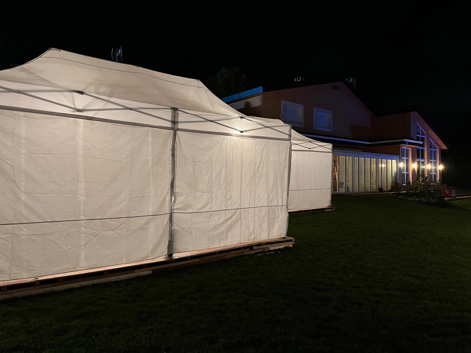Carpas plegables cerradas iluminadas de noche junto a una casa