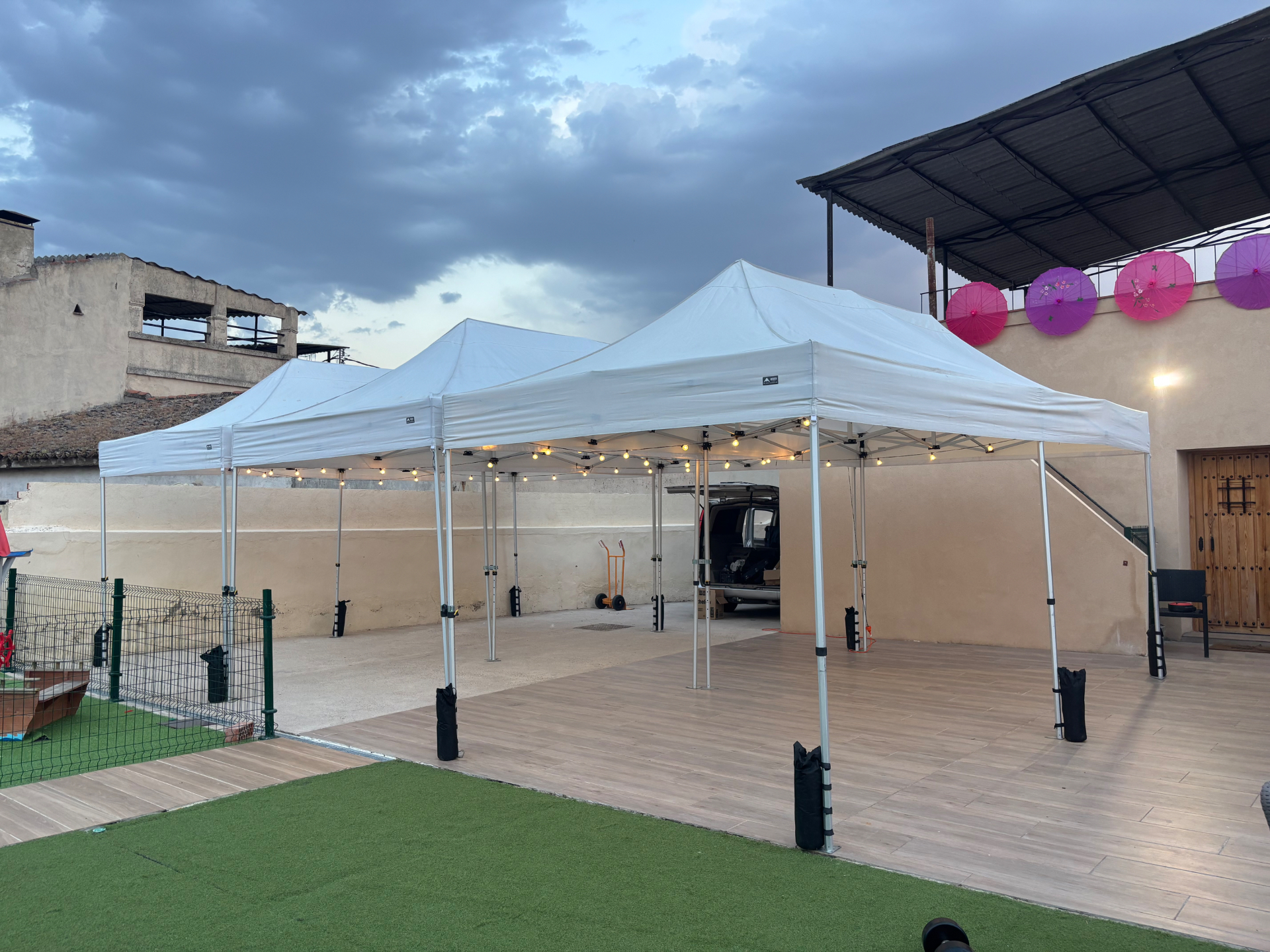 Tres carpas plegables blancas unidas con guirnaldas de luces al atardecer